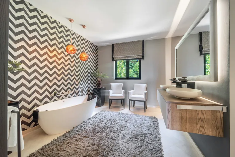 Salle de bains principale avec baignoire îlot, double vasque, suspensions en cuivre et mur à chevrons