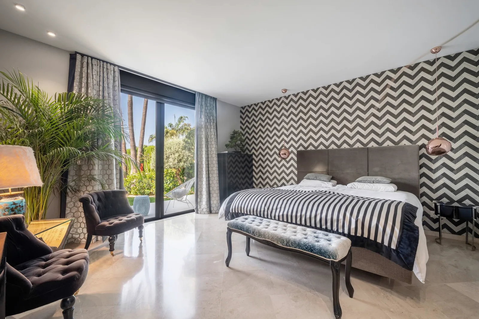 Chambre principale du rez-de-chaussée avec mur à chevrons noir et blanc, dessus-de-lit rayé, banquette en velours et portes donnant sur le jardin