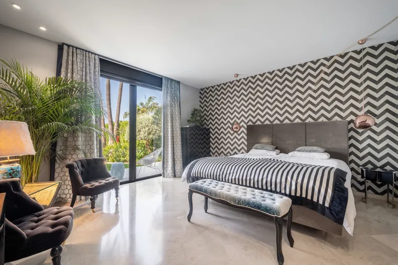 Chambre principale du rez-de-chaussée avec mur à chevrons, dessus-de-lit rayé et portes donnant sur le jardin