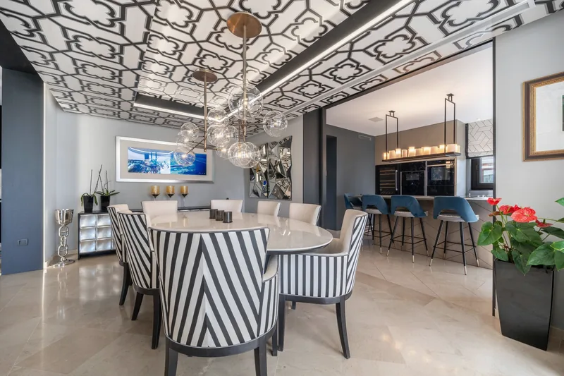 Table de repas pour huit sous un plafond à motifs et un lustre à bulles de verre, ouverte sur la cuisine
