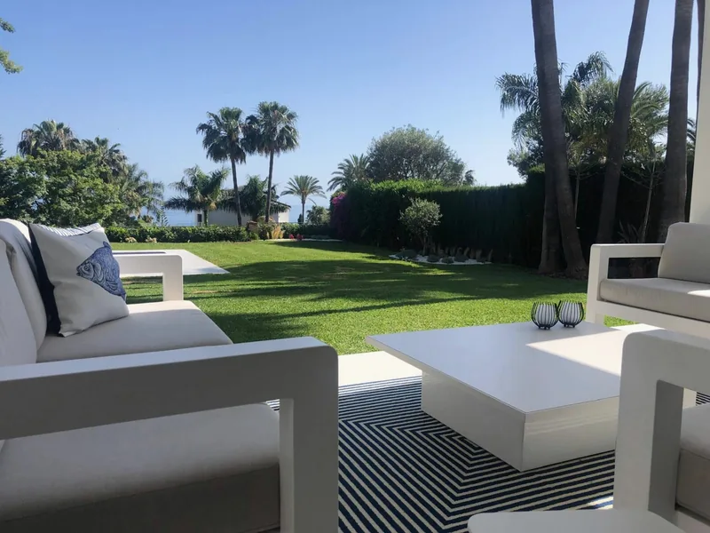 Salon d’extérieur blanc sur la pelouse, avec la mer au loin entre les palmiers