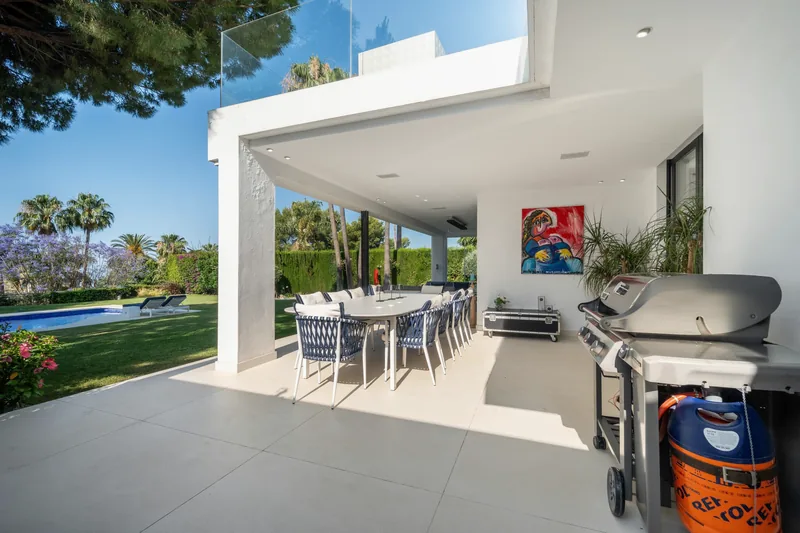 Cuisine d’été avec barbecue à côté de la table de repas de la terrasse, la piscine au-delà