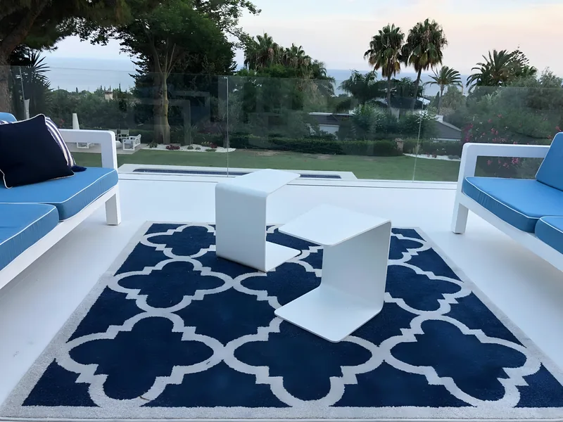 La terrasse panoramique de l’étage au crépuscule, avec coussins bleus et balustrade en verre, face à la mer