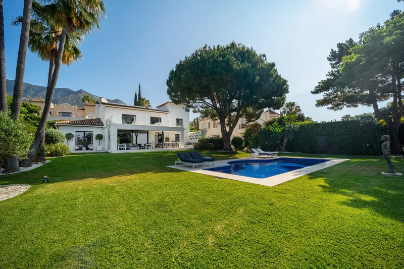 La villa et la piscine depuis le fond de la pelouse, sous les pins parasols